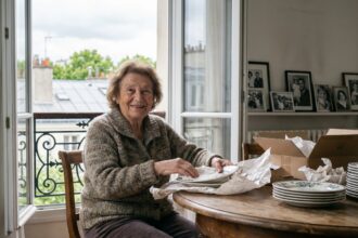 Femme agee souriante emballant des assiettes dans un appartement parisien